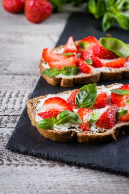 Süzme peynir, fesleğen ve kayrak tahta üzerinde eski püskü ahşap masa arka plan üzerinde çilek çilek bruschetta