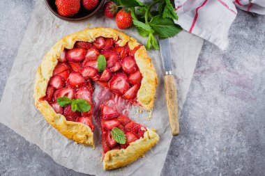 Galette'ye gri Beton taş zemin üzerine çilek ile. Vejetaryen Sağlıklı berry Galette'ye taze dilimlenmiş çilek ve nane ile dekore edilmiştir. Lezzetli yaz tatlı.