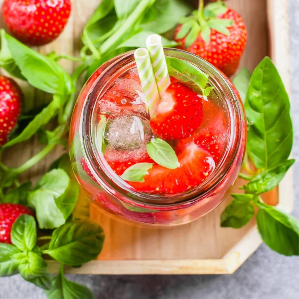 Summer Food and Drink. Strawberry lemonade with basil in mason jar on wooden tray on concrete table. Top view, close-up