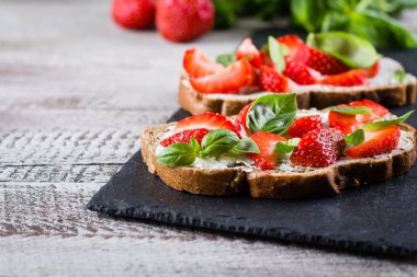 Süzme peynir, fesleğen ve kayrak tahta üzerinde eski püskü ahşap masa arka plan, kopya alanı üzerinde çilek çilek bruschetta
