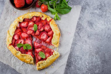 Galette'ye gri Beton taş zemin üzerine çilek ile. Vejetaryen Sağlıklı berry Galette'ye taze dilimlenmiş çilek ve nane ile dekore edilmiştir. Lezzetli yaz tatlı. Üstten görünüm, kopya alanı