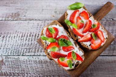 Eski püskü tablo arka plan üzerinde ahşap tahta üzerinde üstten görünüm, süzme peynir, fesleğen ve üzerinde çilek çilek bruschetta. kopya alanı