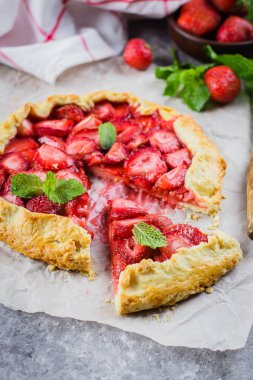 Galette'ye gri Beton taş zemin üzerine çilek ile. Vejetaryen Sağlıklı berry Galette'ye taze dilimlenmiş çilek ve nane ile dekore edilmiştir. Lezzetli yaz tatlı.