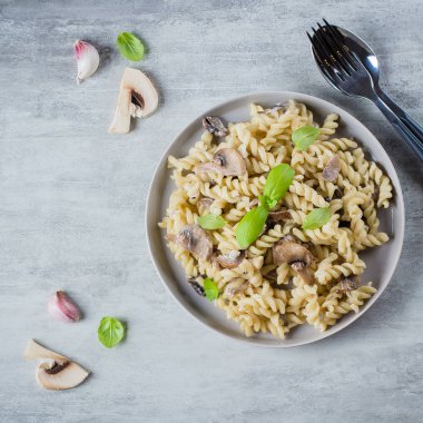 Makarna Fusili mantar, sause krem ve fesleğen taş beton masada. İtalyan gıda kavramı. Üstten görünüm, kopya alanı