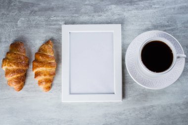 Boş beyaz bir çerçeve ile kopya alanı, fincan kahve ve kruvasan gri tablo arka plan üzerinde. Mockup ile kopya alanı, üstten görünüm