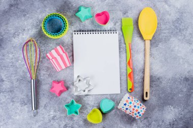 Gri beton tablo arka plan üzerinde renkli gökkuşağı mutfak gereçleri ve boş defter üstten görünüm. 