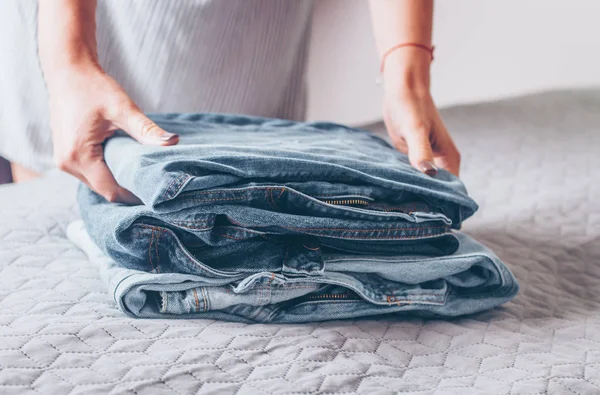 女性は ベッドの上のグレーのカバーのジーンズを折る ブルー ジーンズ服の山 — ストック写真