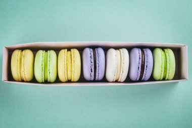 Pasta macaron veya yukarıdan yeşil renkli kağıt kutusunda acıbadem kurabiyesi. Renkli badem çerezler, pastel renkler. Üstten görünüm, düz yatıyordu