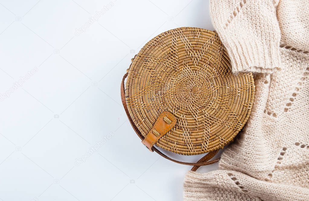 Fashionable rattan bag and cozy beige sweater on light background