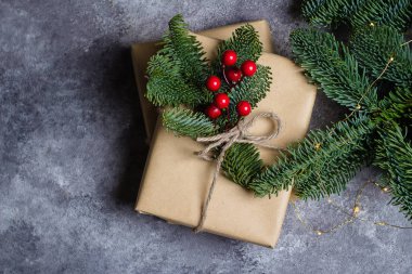 Noel hediye kutusu Kraft kağıt tarafından sarılmış ve köknar dalı ve beton tablo arka plan üzerinde kırmızı dut tarafından dekore edilmiştir. Noel hediyeleri ve kış tatil kavramı. Düz kopya alanı ile yatıyordu.