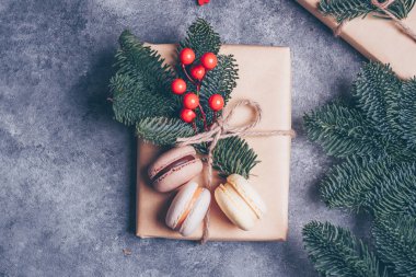 Noel hediye kutusu Kraft kağıt tarafından sarılmış ve köknar dalı, kırmızı berry ve tatlı macaroons beton tablo arka plan üzerinde tarafından dekore edilmiştir. Noel hediyeleri ve kış tatil kavramı. Düz kopya alanı ile yatıyordu.
