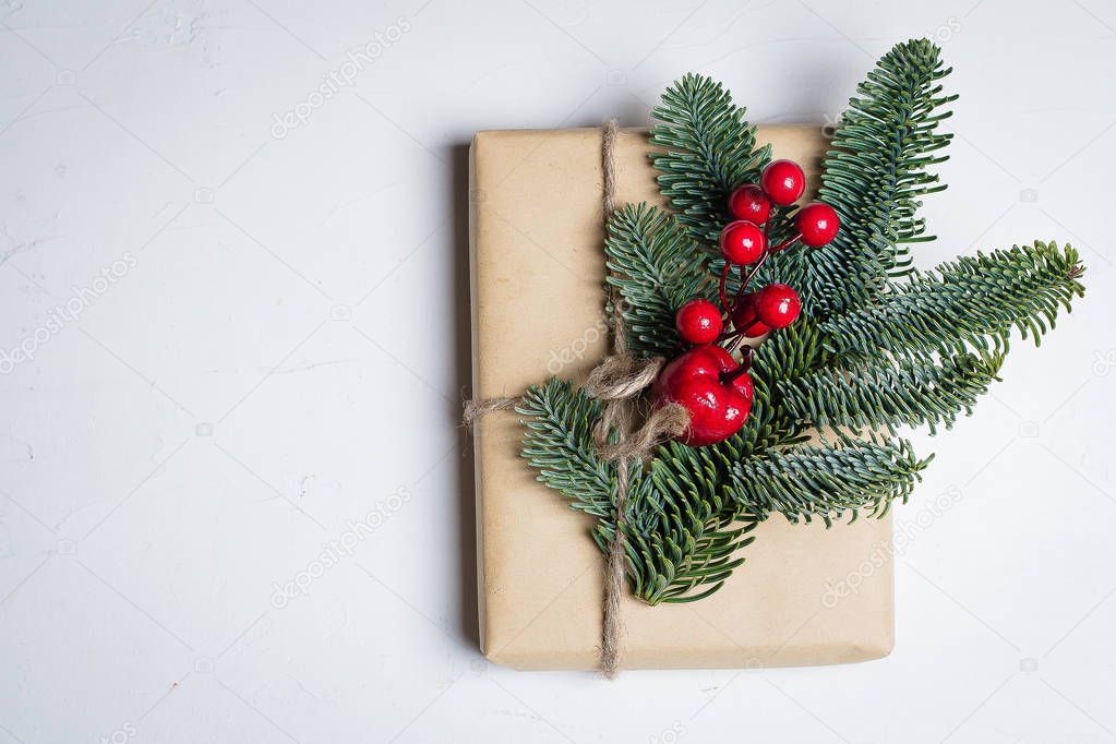 Christmas Gift box wrapped by craft paper and decorated fir branch and red berry decoration on a table background. The concept of Christmas presents and winter Holidays. Flat lay with copy space.
