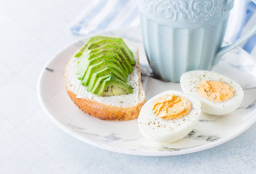 Healthy vegan breakfast concept. Whole grain bread sandwiches with avocado and boiled eggs on plate and mug of black coffee on blue table background. Clean eating