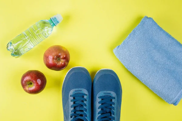 Flat Lay of blue sneakers, towel, red apple and water bottle on yellow background. Sport equipment. Concept of healthy lifestile. Top view, copy space