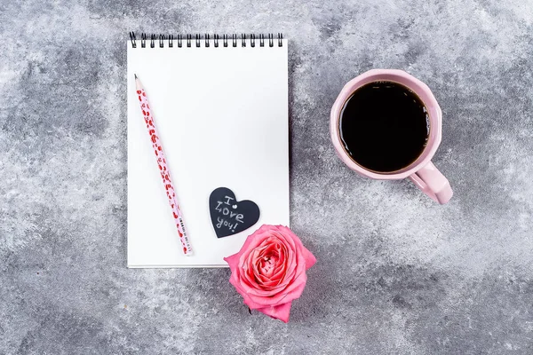 Cup of black coffee, open notebook, rose and black hearts on gray background, copy space. Minimal flat lay with coffee and mock up book for Valentine day text, love and romance concept, top view.