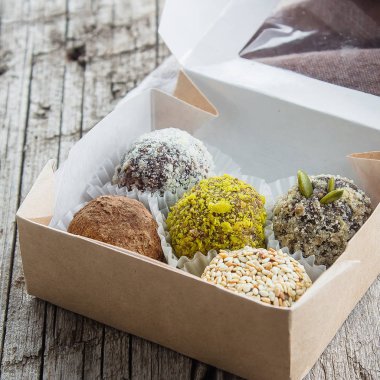 Kurutulmuş meyve ve fındık Hindistan cevizi cips, kakao, keten tohumu, fıstık, susam ile sağlıklı enerji toplar yaptı. Ahşap masa kağıt kutusunda çiğ vegan şeker