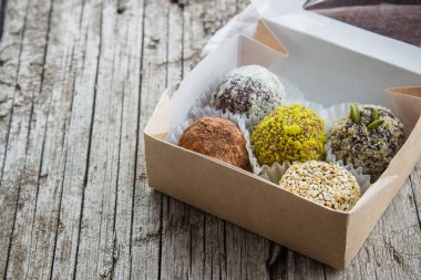 Kurutulmuş meyve ve fındık Hindistan cevizi cips, kakao, keten tohumu, fıstık, susam ile sağlıklı enerji toplar yaptı. Ahşap masa kağıt kutusunda çiğ vegan şeker
