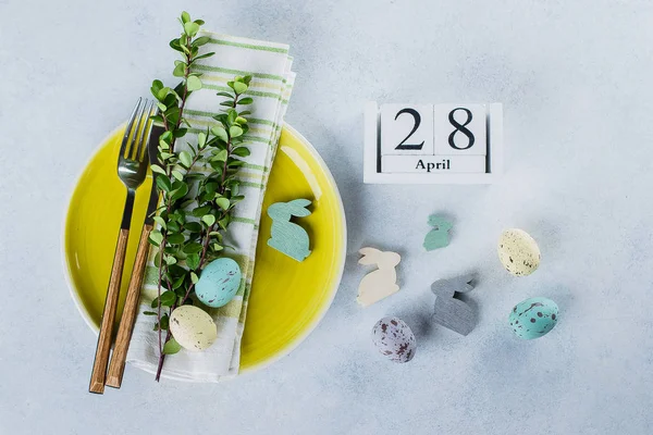 Festive table setting for holiday Easter dinner on light concrete table with copyspace. Spring Holiday Card Concept. Calendar 28 april date