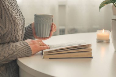 Erkek Close-Up holding fincan çay ya da kahve açık kitap önünde eller. Beyaz masa iç. Cozy ruh ev kavramı