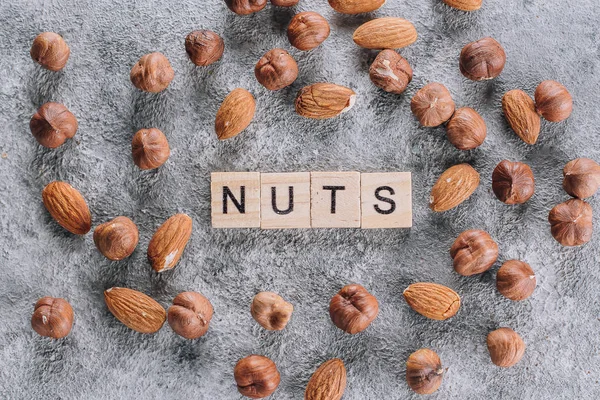 Almendras y avellanas. Surtido Mezcla de tuercas sobre fondo de mesa de hormigón gris. Letras de madera Word Nuts. Vista superior — Foto de Stock