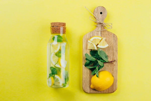 Limón Agua de menta o limonada en botella de vidrio e ingredientes sobre tablas de cortar de madera sobre fondo de mesa amarillo. Concepto de bebida de verano — Foto de Stock