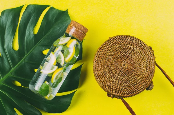 Round rattan bag and glass bottle with lemonade on a Monstera le