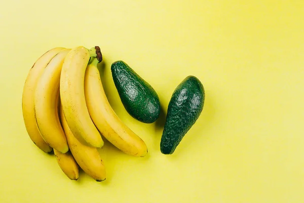 Bananas and avocado on the yellow background. Top view, copy space
