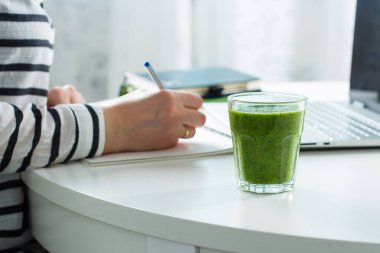 Ev ödevi Freelancer kavramı. Kadın defter, laptop yakın tarih yazma. Sağlıklı Yeşil Smoothie fromspinach, kivi ve elma