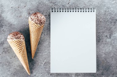 Çikolatalı dondurma waffle koniler ve üstünde gri tablo arka plan beyaz boş boş defter. Yaz tatlı tarifi kavramı. Üstten Görünüm