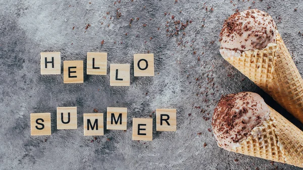 Banner beeld. Chocolade-ijs in wafel kegels en tekst in kleine houten lettertjes Hallo zomer op betonnen grijze tabelachtergrond. Bovenaanzicht — Stockfoto