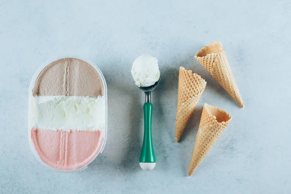 Ice cream box, spoon with ice-cream ball and three waffle cones.