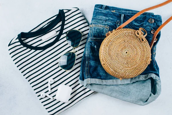 Spring and summer women's clothing and accessories. Striped t-shirt, blue denim shorts and fashionable organic rattan bag. Flat lay photo, top view — Stock Photo, Image