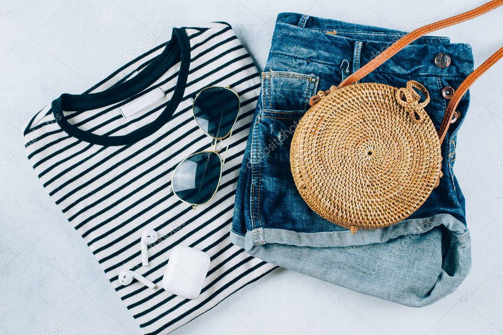 Spring and summer women's clothing and accessories. Striped t-shirt, blue denim shorts and fashionable organic rattan bag. Flat lay photo, top view