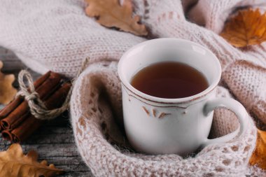 Ahşap bir tahta masa arka plan üzerinde sıcak örme kazak ve sıcak çay fincan. Mood Cozy İçecek Kavramı