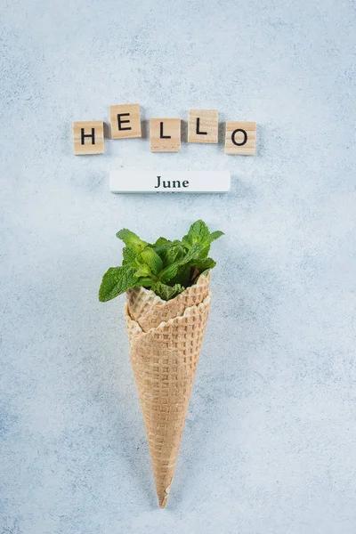 Ice Cream wafel kegel met mint bladeren op blauwe achtergrond. Dessert, zomerkaart concept. Houten letters Word Hallo juni. Bovenaanzicht, vlakke lay. — Stockfoto