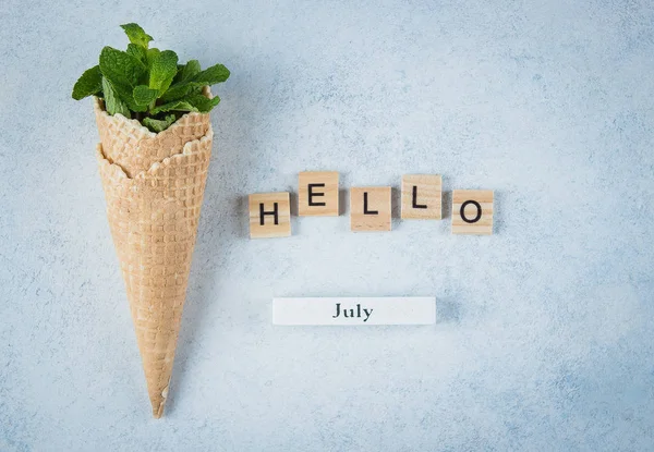 Ice Cream wafel kegel met mint bladeren op blauwe achtergrond. Dessert, zomerkaart concept. Houten letters Word Hello juli. Bovenaanzicht, vlakke lay. — Stockfoto