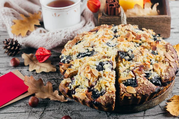 Cozy Autumn Food. Homemade autumn cake with nuts and plums and empty paper card for text on wooden background, Top view, copy space.
