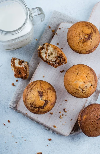 Muffin dolci fatti in casa alla vaniglia al cioccolato di due tipi di pasta con barattolo di latte su tavola di legno su sfondo blu tavolo di pietra — Foto Stock