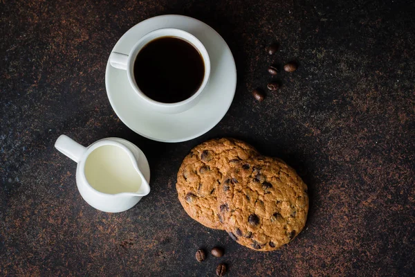 Kahve bardağı ve koyu taş beton masa arka plan üzerinde çikolatalı kurabiye ile süt. Sabah Kahvaltısı Konsepti. Kopyalama alanı