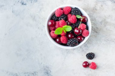 Gri beton masa arka plan üzerinde beyaz kase yaz taze çilek. Kopyalama alanı ile üst görünüm. Vejetaryen gıda - ahududu, böğürtlen ve kiraz