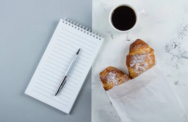 Taza de café con croissants y cuaderno vacío y pluma para el plan de negocios y las ideas de diseño sobre fondo bicolor desde arriba. Plan matutino. Plano concepto laico — Foto de Stock