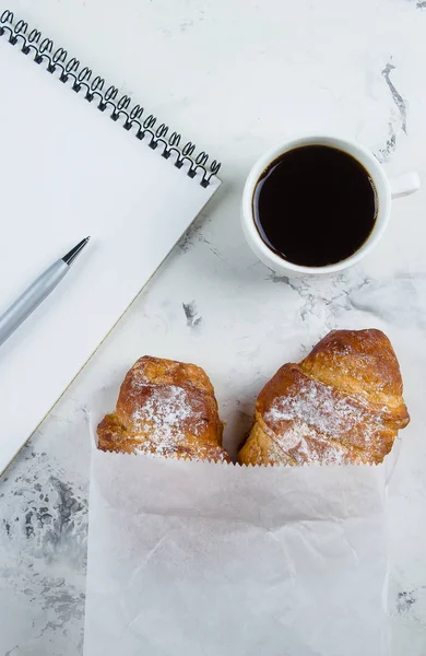 Taza de café con croissants y cuaderno vacío y pluma para el plan de negocios y las ideas de diseño sobre fondo de mármol desde arriba. Plan matutino. Plano concepto laico — Foto de Stock