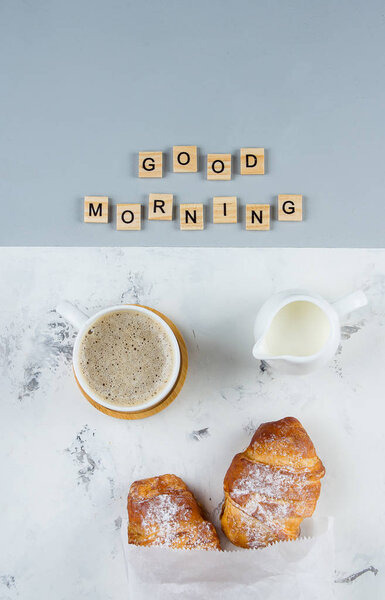 Good Morning Breakfast Minimal Concept. Cup of coffee, croissant and text Good Morning on pink gray background. Flat lay