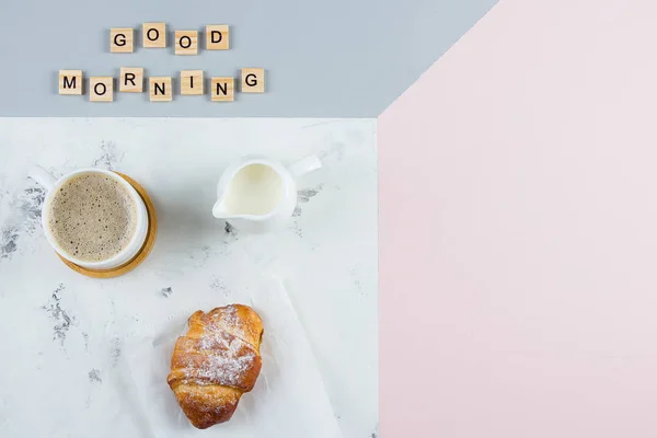God morgon frukost minimalism koncept. Kopp kaffe, croissant och text god morgon på tricolor bakgrund. Flat Lay, kopiera utrymme — Stockfoto