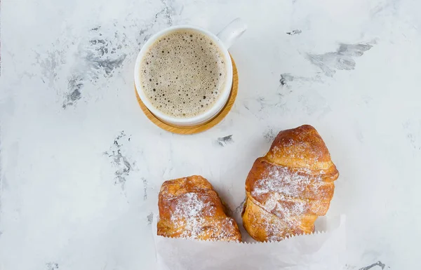 Dva čerstvé croissanty v papírovém pytli a šálku kávy na mramorovém pozadí, vrcholové zobrazení, kopírovací prostor, plochý ležel — Stock fotografie