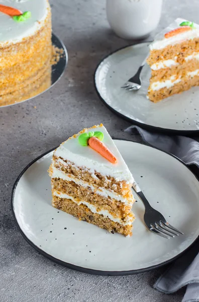 Slice of homemade carrot cake with cream cheese frosting on plate on gray stone table background