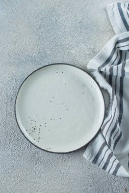 Açık taş beton masa arka plan üzerinde boş seramik plaka ve mutfak çizgili havlu. Kopya alanı. Menü Tarifi Kavramı. Üst te. Düz yatıyordu