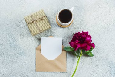 Kahvaltı için sabah kahve fincanı, mevcut kutu veya hediye, boş nota, kart ve açık taş masada pembe şakayık çiçekler. Düz döşeme stilinde üst görünüm, kopyalama alanı