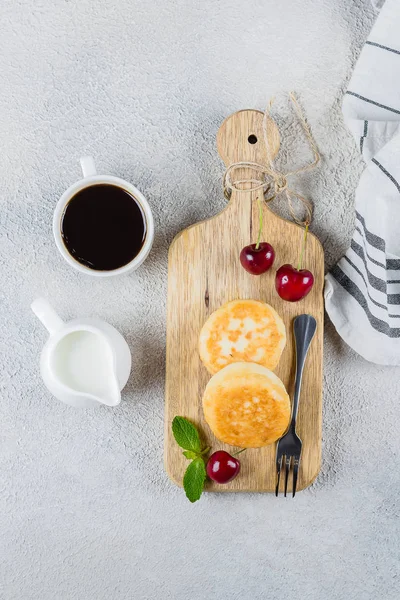 Завтрак Еда Вкусная концепция. Оладьи с сыром на разделочной доске с вишней, чашка кофе с молоком на фоне каменного стола. Вид сверху, пространство для копирования — стоковое фото
