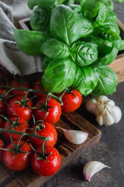 Koyu browm beton taş arka plan üzerinde kesme tahtası üzerinde fesleğen ve sarımsak ile Organik Kiraz Domates. Üstte görüntü